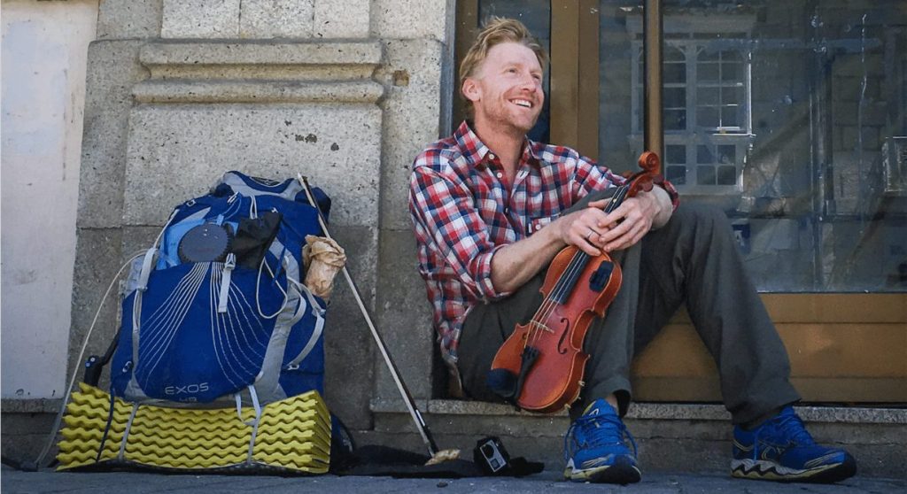 Alastair Humphreys in doorway with rucksack and violin