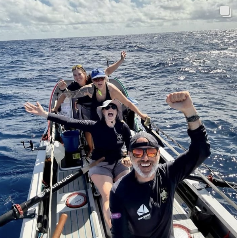 4 person rowing team from Atlantic Fusion smiling and raising hands in celebration while out on the open sea